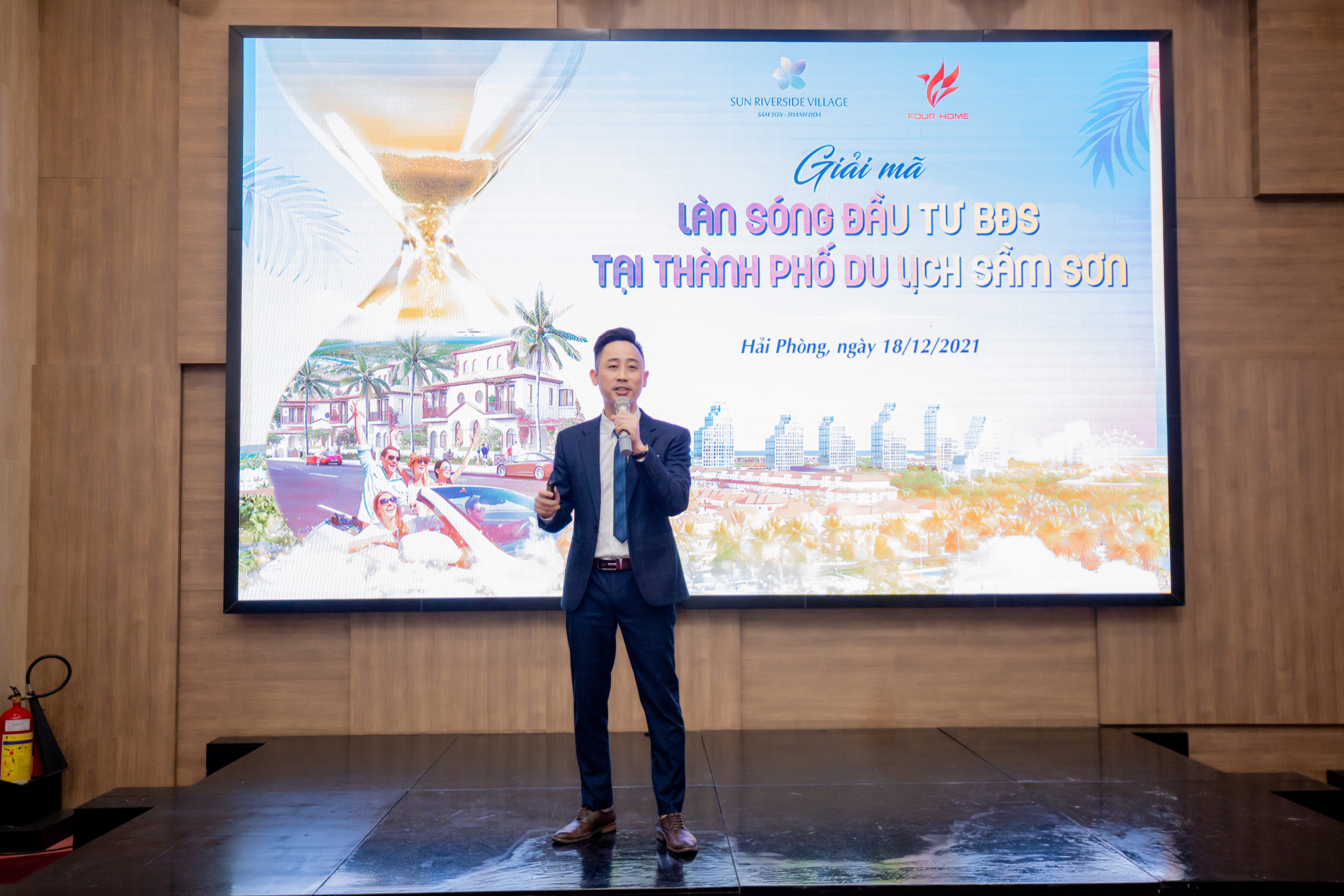 Đăng Dương cầm micro thuyết trình trên sân khấu trước màn hình lớn giới thiệu dự án bất động sản cho nhà đầu tư