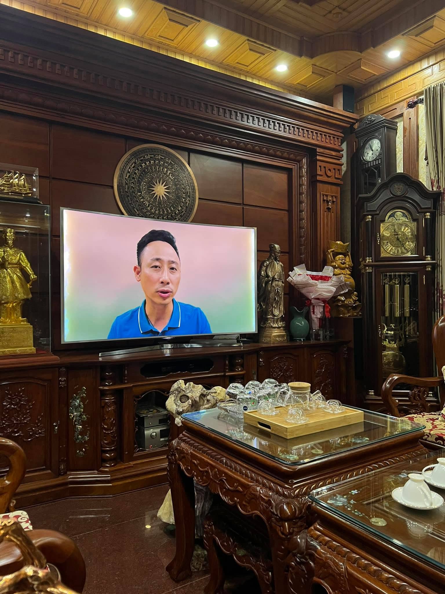 Màn hình tivi trong phòng khách nhà khách hàng đang phát video của một môi giới bất động sản, xung quanh là nội thất gỗ