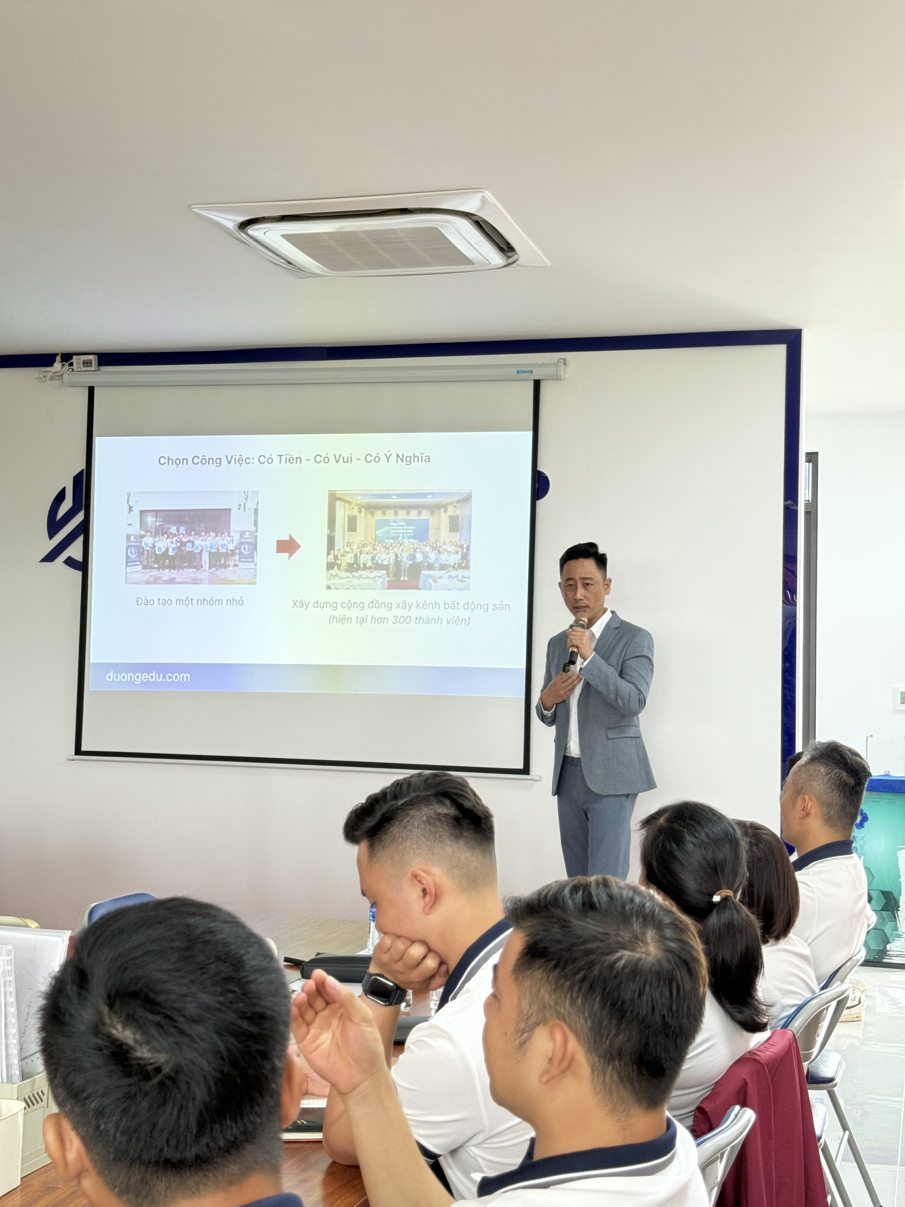 Đăng Dương mặc vest xám hai tay cầm micro trước ngực, sau lưng là màn chiếu nói về việc chọn một công việc vừa có tiền, vừa có niềm vui, vừa có ý nghĩa