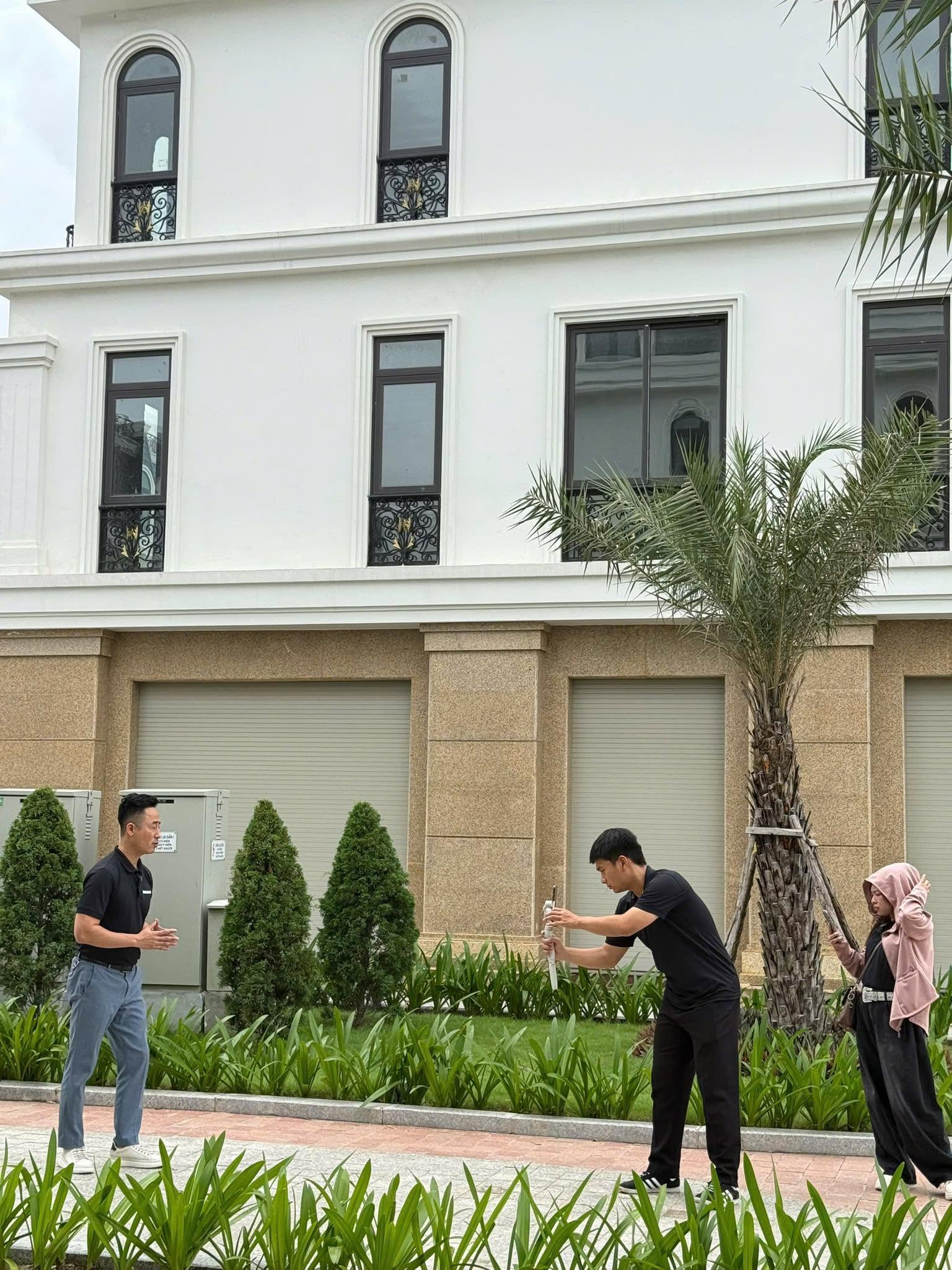 Một người đàn ông đứng nói trước khu nhà liền kề mới xây, hai người khác đang quay bằng điện thoại và cầm đèn