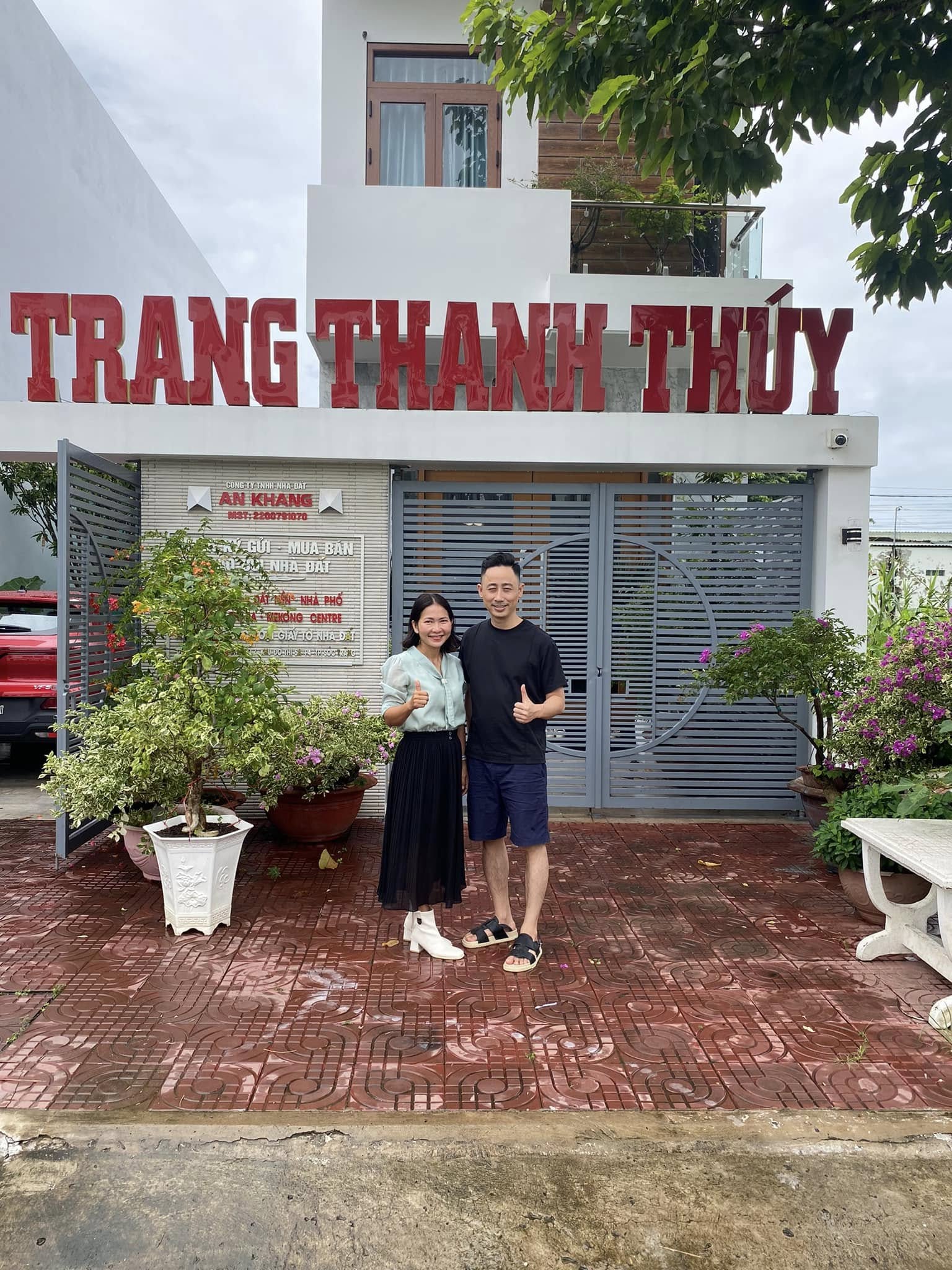 Đăng Dương và một học viên nữ giơ ngón tay cái trước văn phòng nhà đất có biển hiệu tên học viên
