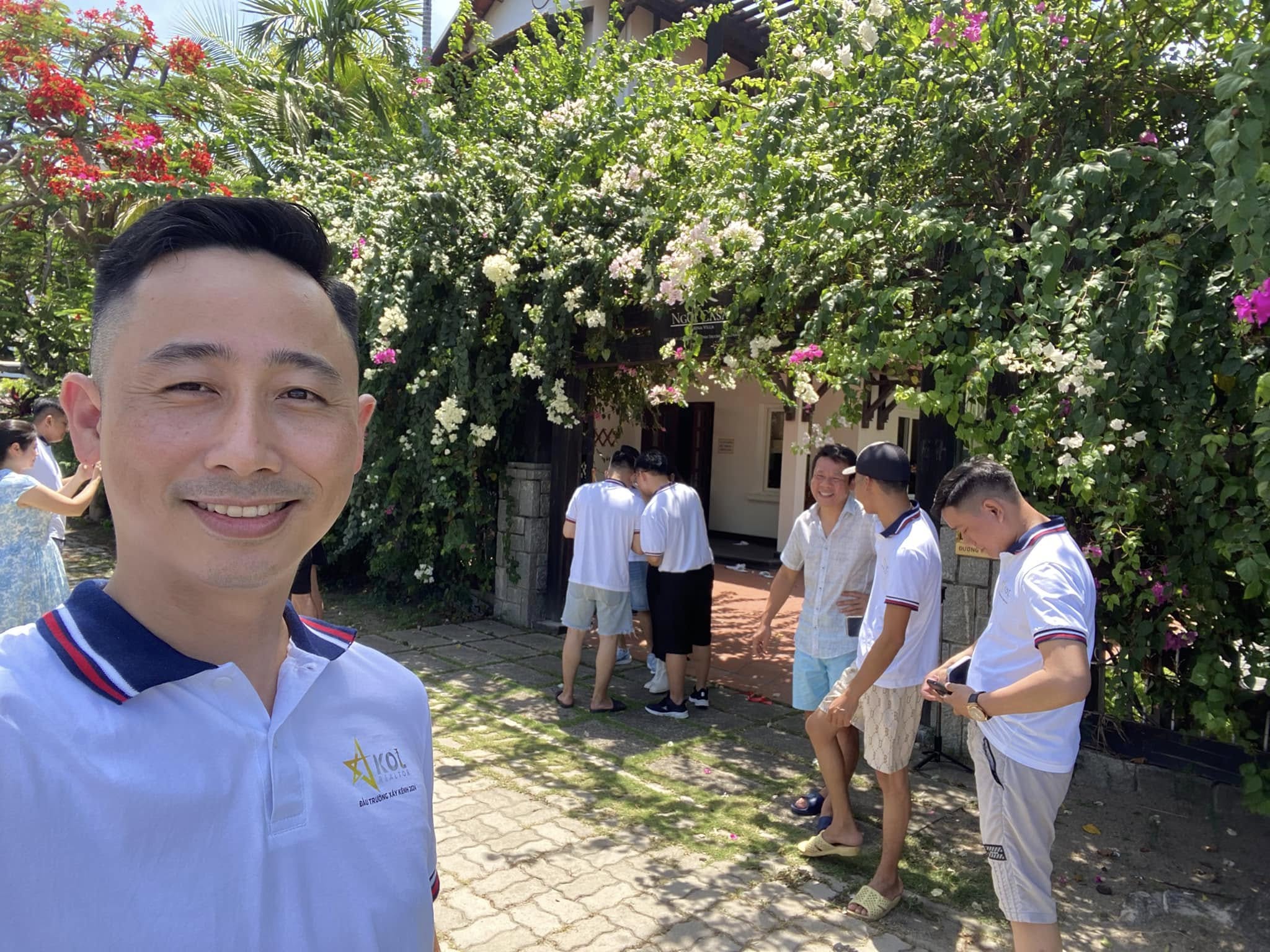 Đăng Dương chụp ảnh selfie trong áo polo trắng in chữ Đấu trường xây kênh, phía sau là nhóm người mặc áo cùng loại