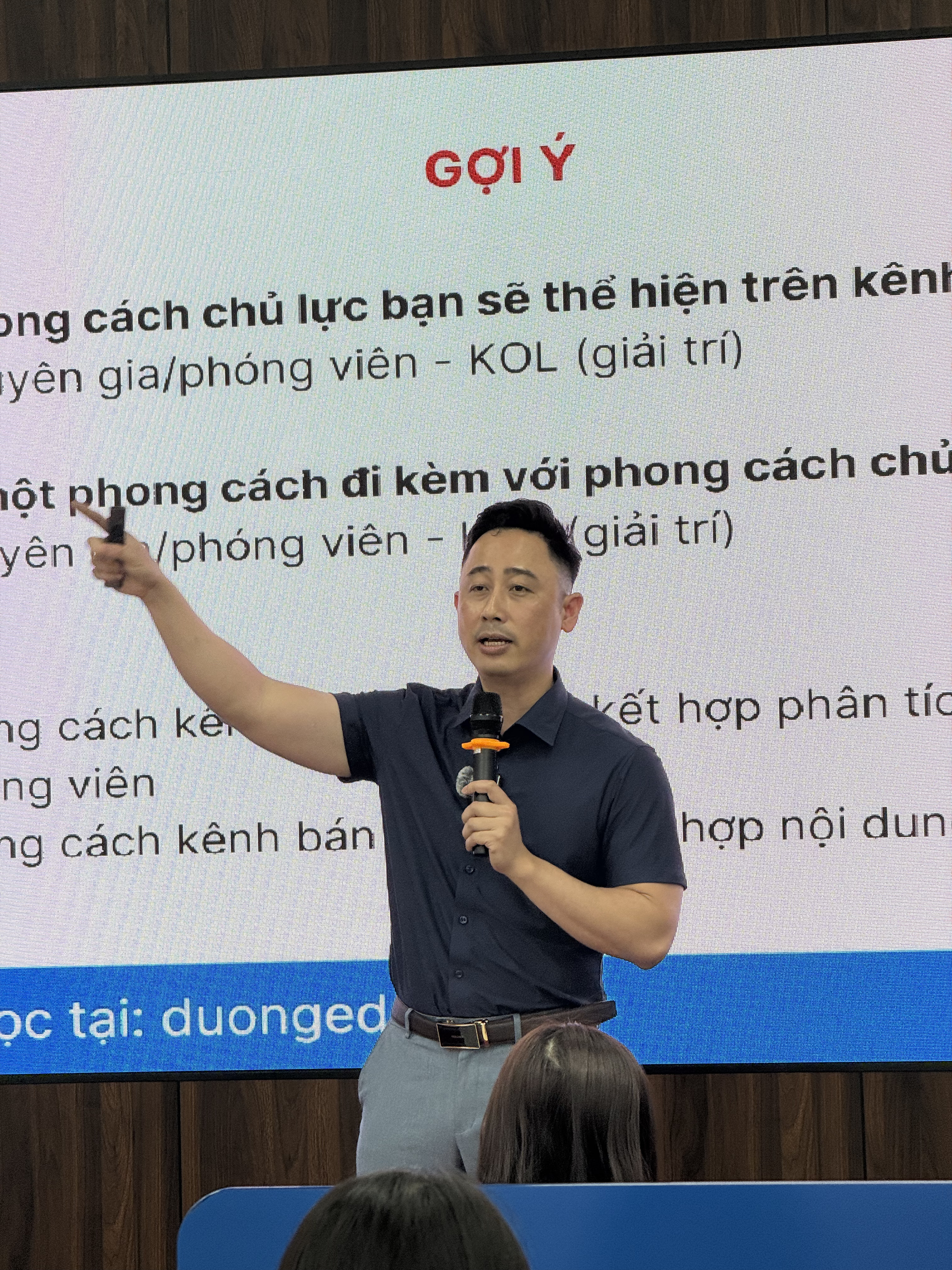 Đăng Dương đứng phía xa chỉ lên màn hình chiếu gợi ý chọn phong cách kênh