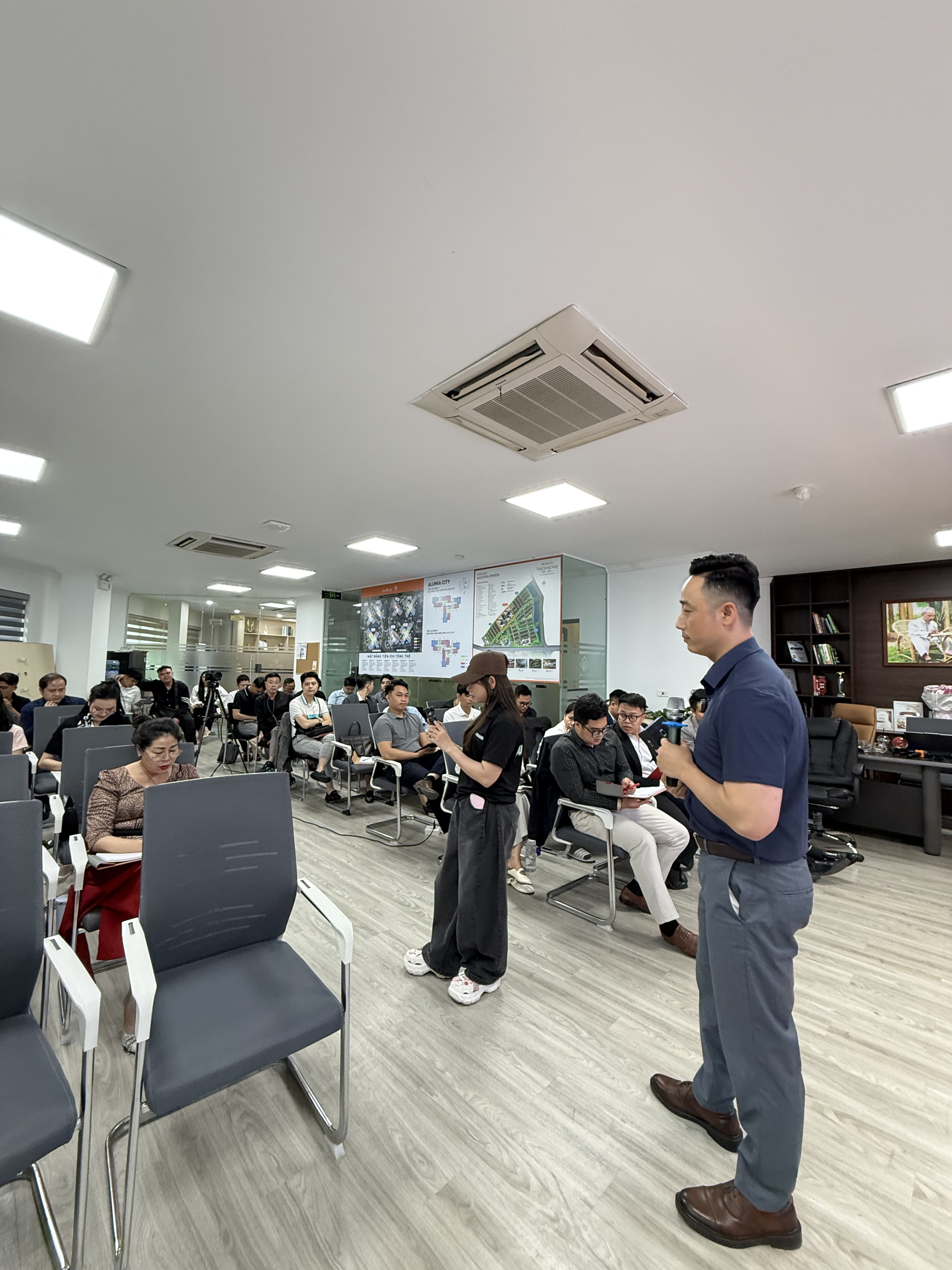 Đăng Dương đứng giữa hàng ghế học viên trong buổi đào tạo tại sàn, phía sau là tủ trưng bày cúp