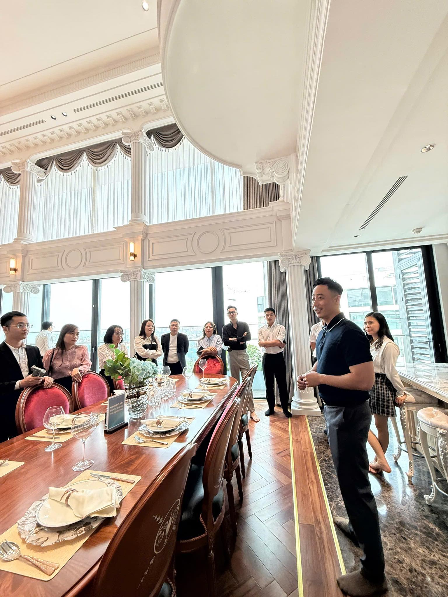 Đăng Dương mặc áo polo đen đứng trao đổi với một nhóm người bên bàn ăn dài trong căn hộ mẫu cao cấp