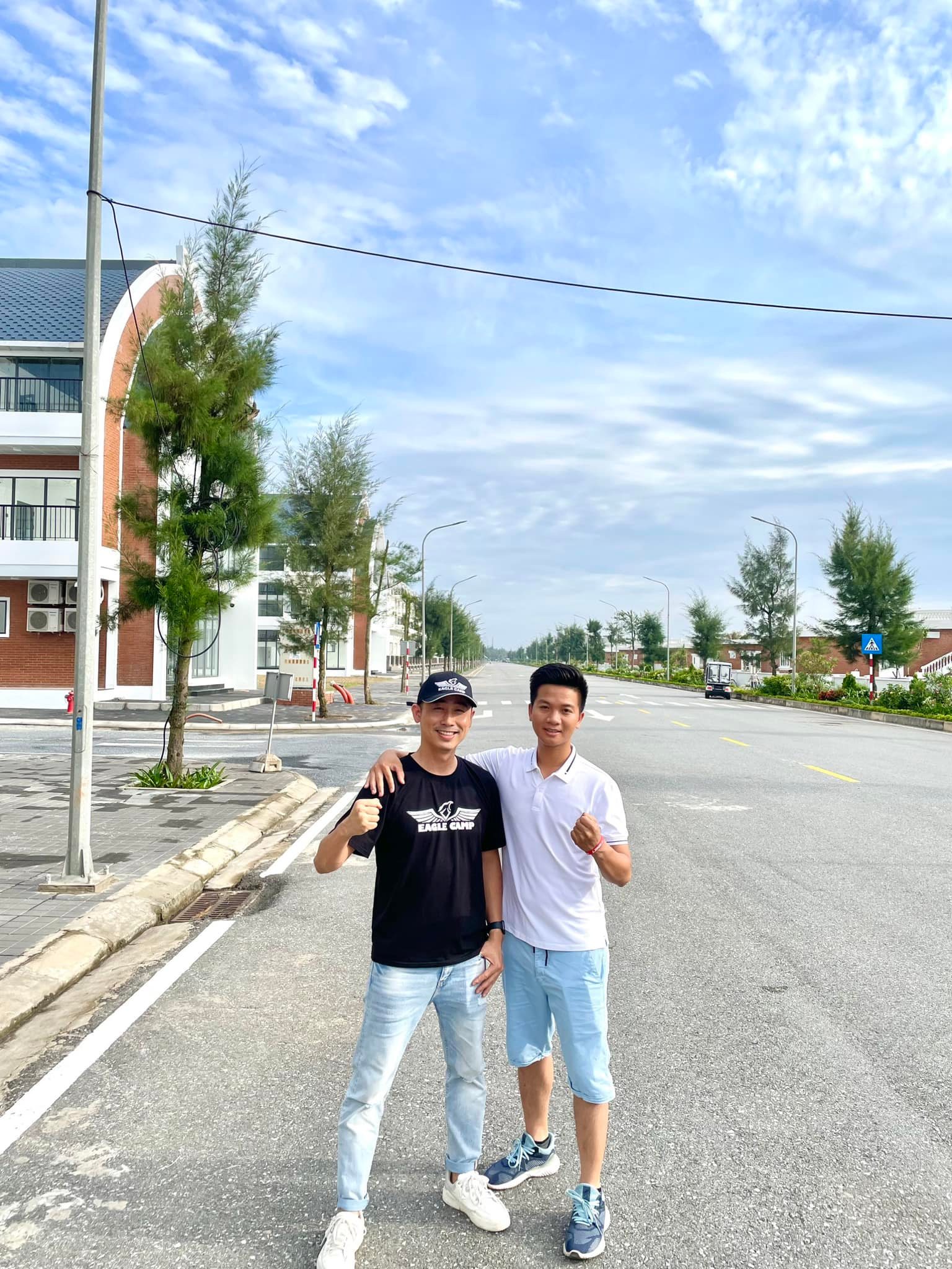 Đăng Dương mặc áo phông đen chụp ảnh cùng một người mặc áo polo trắng giữa con đường lớn trong khu đô thị ven biển